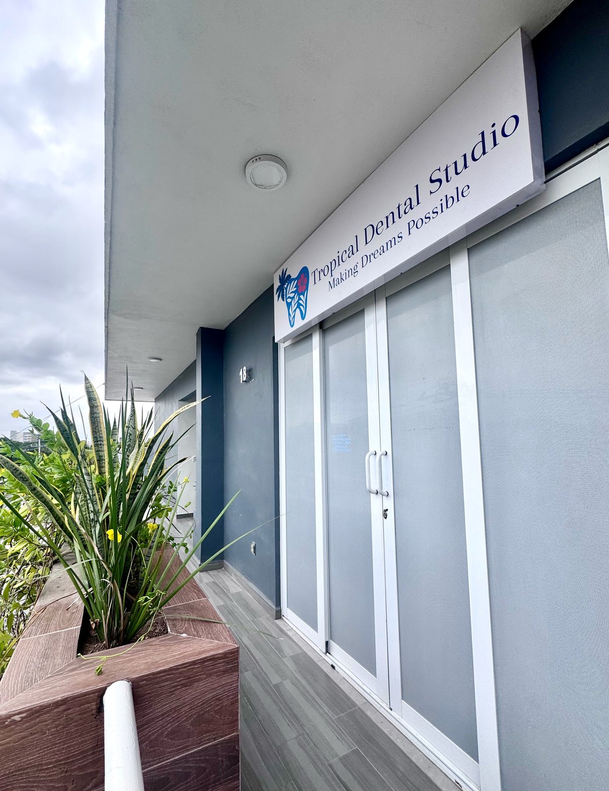 Fachada de Tropical Dental Studio con puertas de vidrio y fachada azul oscuro